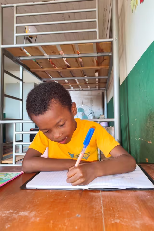 Un enfant de Malaza en t-shirt jaune écrit dans son cahier pendant le temps de soutien scolaire