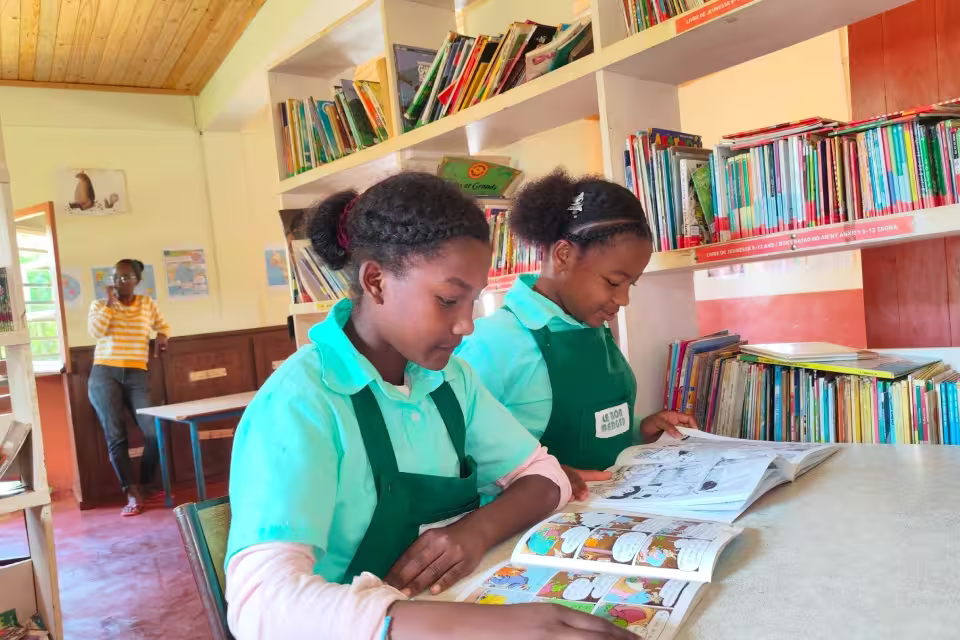 Deux collégiennes de Malaza lisent côte à côte à la bibliothèque, devant les rayonnages de livres