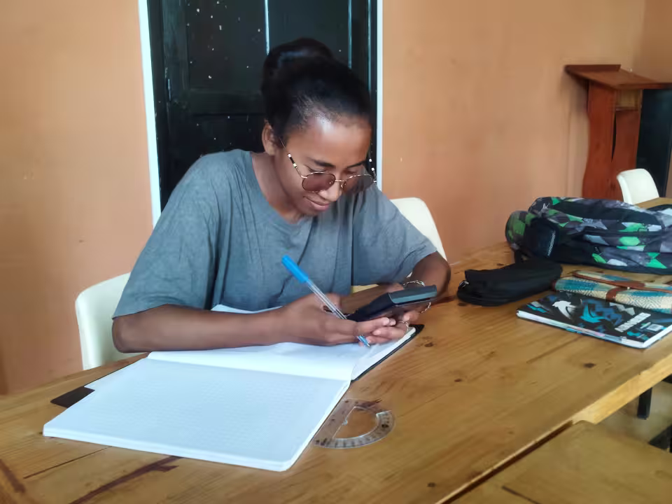 Une adolescente accompagnée par Aïna révise ses cours, cahier et calculatrice posés devant elle