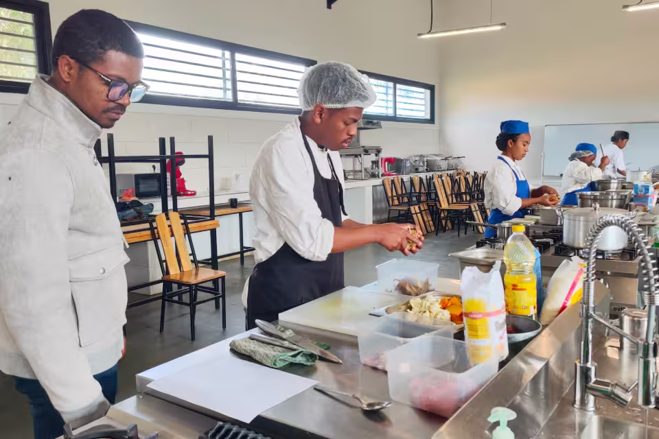 Un élève de l'École de Cuisine Solidaire prépare ses ingrédients en cuisine pédagogique sous l'œil de son formateur