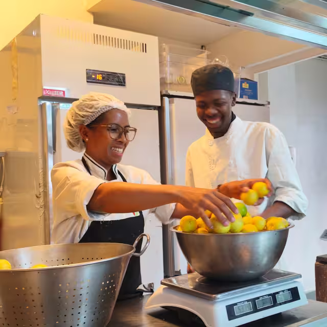 Deux élèves de l'École de Cuisine Solidaire pèsent des agrumes avant la préparation