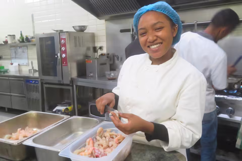 Une stagiaire de l'École de Cuisine Solidaire prépare des crevettes dans la cuisine d'un établissement partenaire