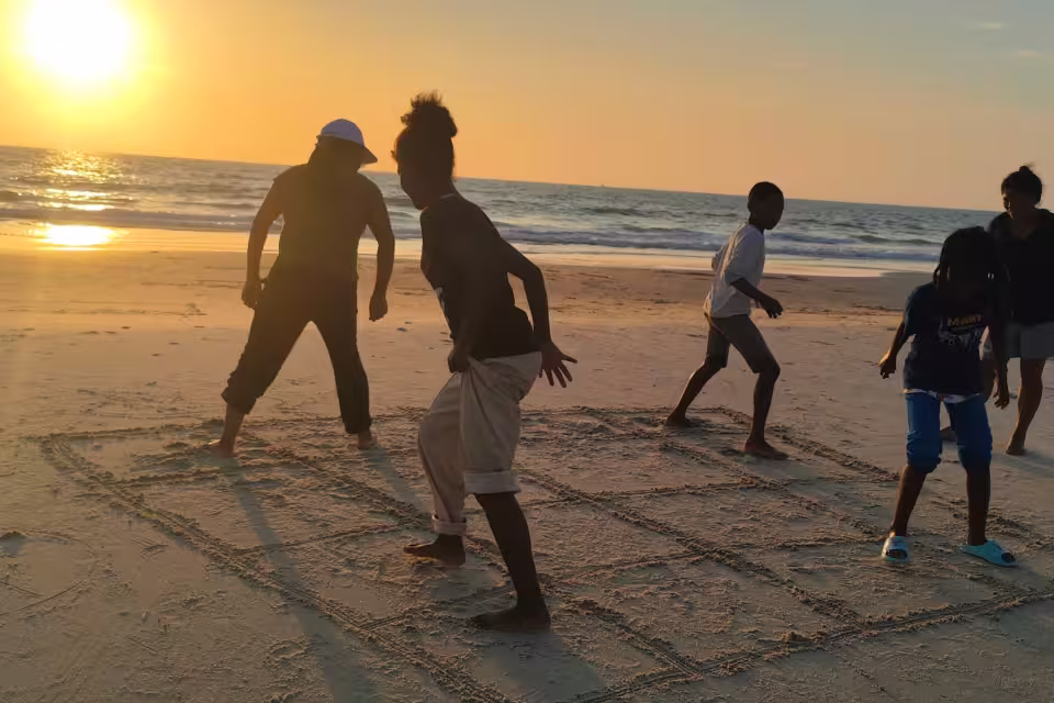 Des enfants jouent à la marelle tracée dans le sable, face au soleil couchant