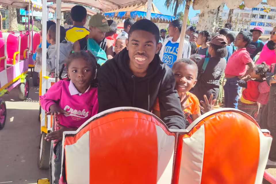 Un jeune de la Maison des Jeunes et deux enfants de Malaza sourient à bord du petit train d'Antsirabe