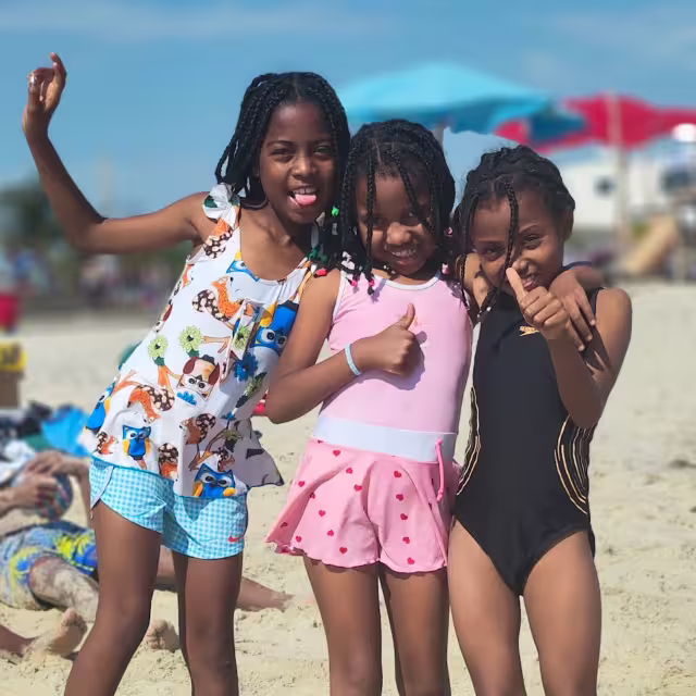 Trois fillettes de Malaza en maillot de bain sourient sur le sable de la plage