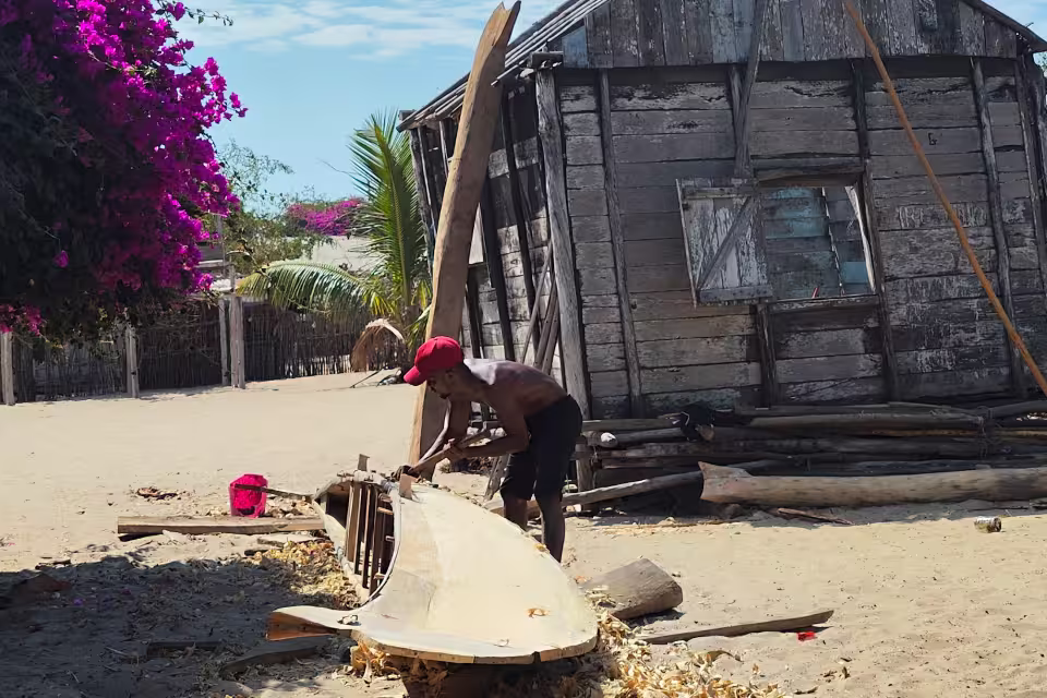 Un artisan du village de pêcheurs façonne une pirogue en bois devant sa maison