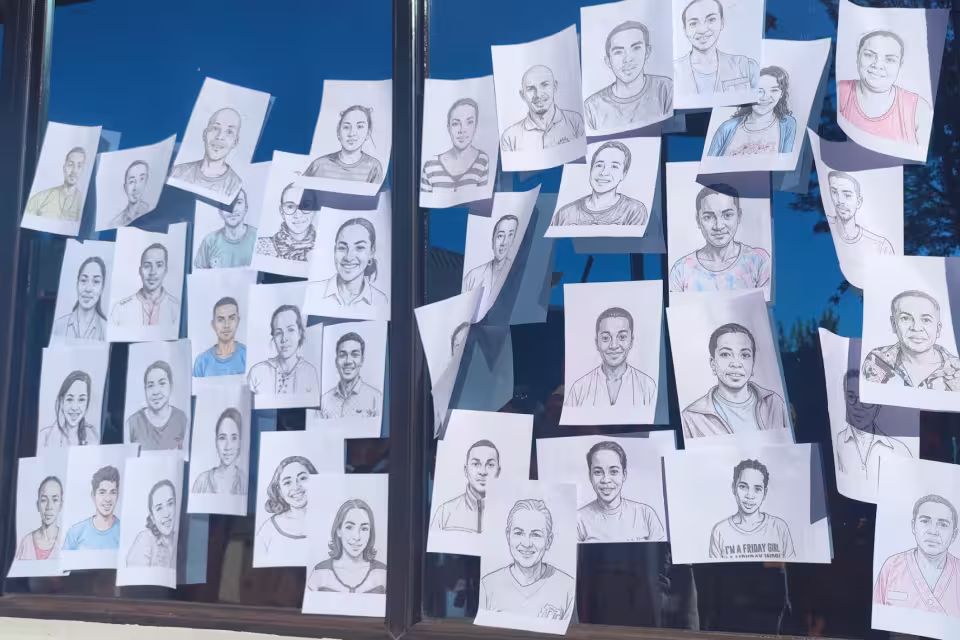 Portraits dessinés des membres du personnel d'Aïna affichés sur les vitres du Village Aïna