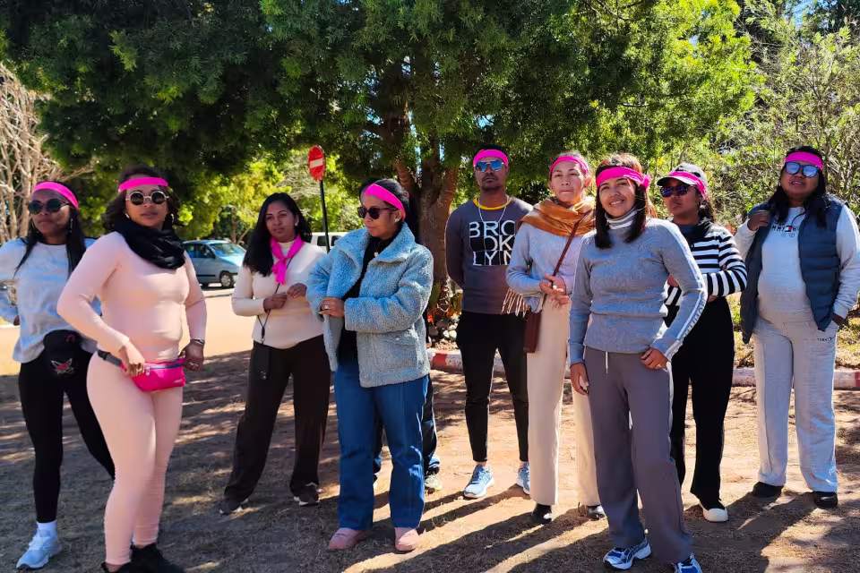 Un groupe de salariées d'Aïna portant un bandeau rose, réunies sous les arbres du Village Aïna