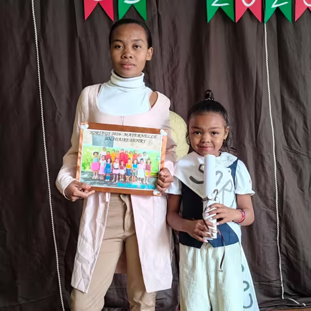 Une éducatrice et une élève de Grande Section posent avec le tableau souvenir de la promotion 2026 de la maternelle solidaire d'Isotry