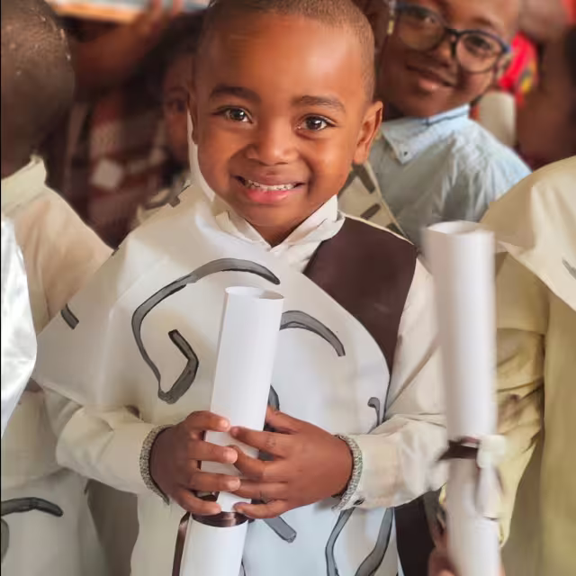 Un enfant de Grande Section sourit en tenant son certificat de scolarité roulé