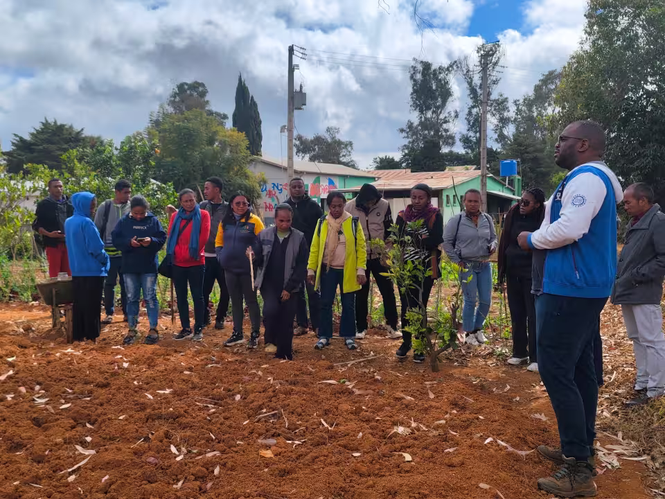 Les participants à la formation REAP réunis autour du formateur devant une parcelle cultivée du Centre de Formation Agricole d'Aïna