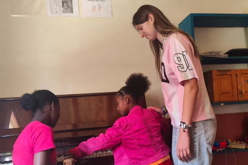 Une lycéenne de Marseille accompagne deux enfants de Malaza au piano lors d'un atelier musical